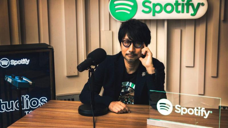 Hideo Kojima yanında ve altında Spotify logolarıyla oturuyor
