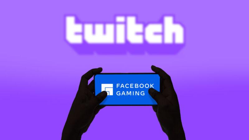Someone is holding a mobile phone that shows Facebook Gaming logo, rest is purple background with a blurred Twitch logo that dominates the image