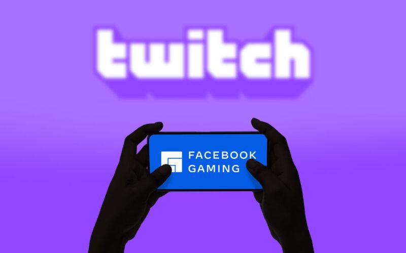 Someone is holding a mobile phone that shows Facebook Gaming logo, rest is purple background with a blurred Twitch logo that dominates the image
