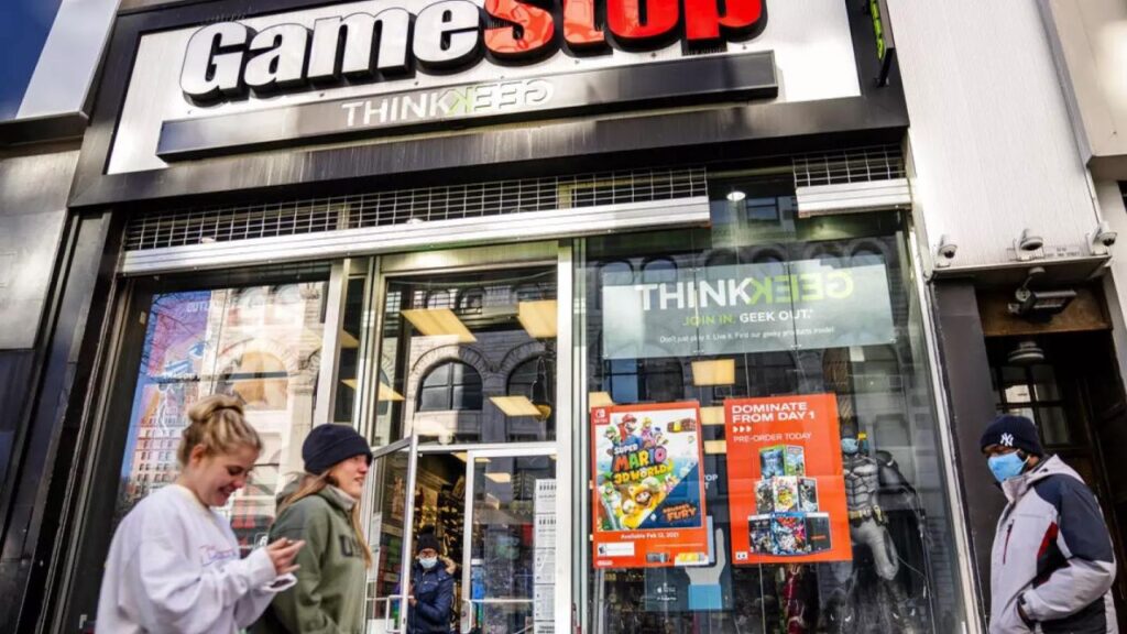 GameStop mağazası önünde yürüyen iki kadın ve bir erkek.