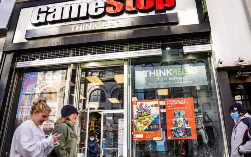 GameStop mağazası önünde yürüyen iki kadın ve bir erkek.