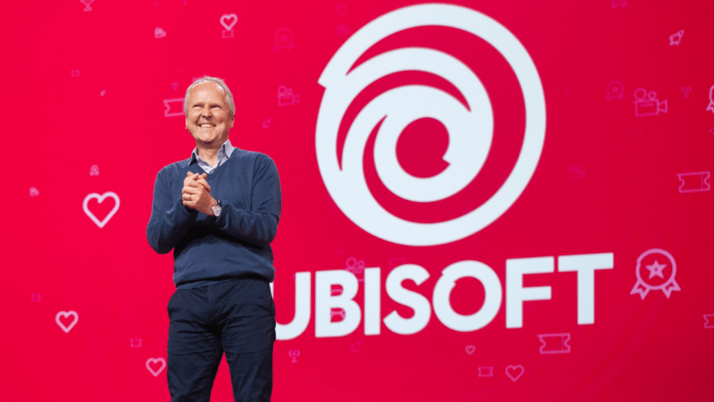 Ubisoft CEO Yves Guillemot giving a speech in front of the Ubisoft logo over red background