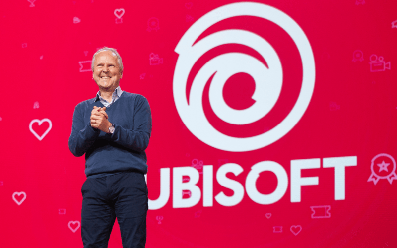 Ubisoft CEO Yves Guillemot giving a speech in front of the Ubisoft logo over red background