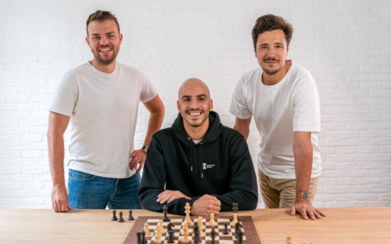 Masa üzerinde bir satranç tahtası ve arkada Immortal Game kurucu ortakları