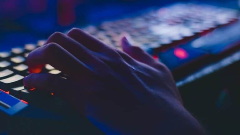 young person's hand over a keyboard in a dark room.