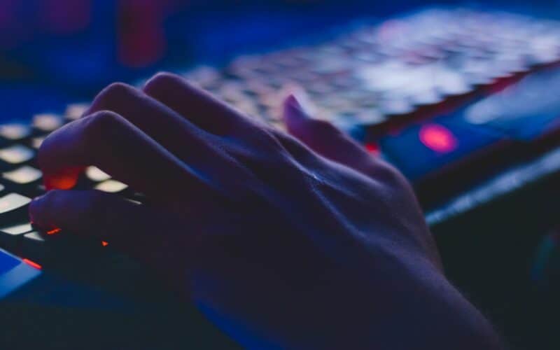 young person's hand over a keyboard in a dark room.