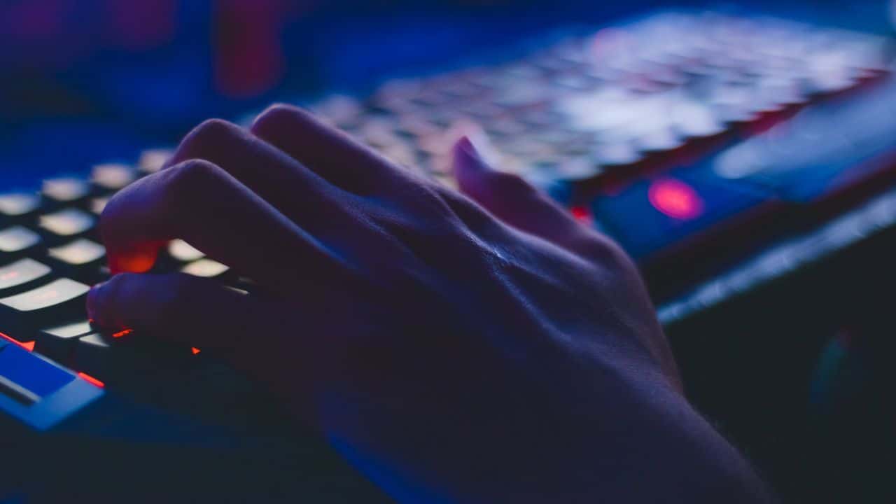 young person's hand over a keyboard in a dark room.