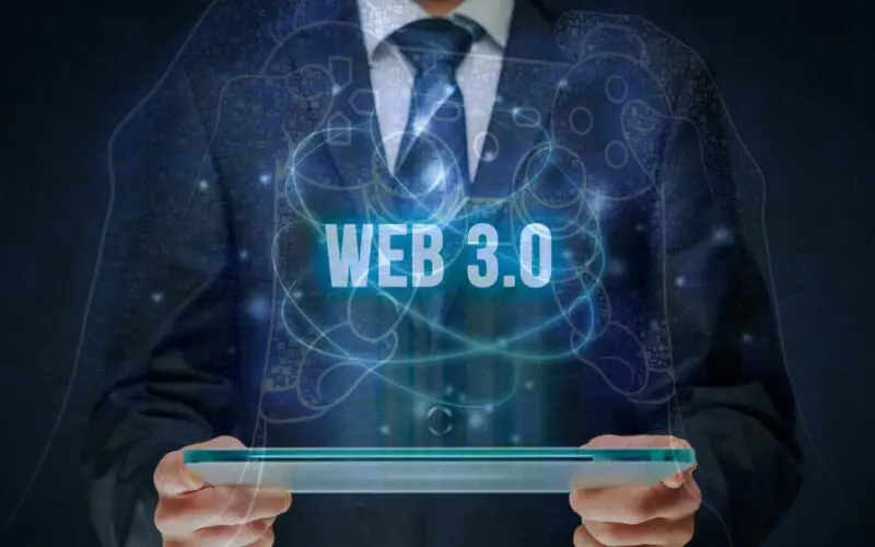 elinde akıllı cihaz tutan takım elbiseli bir kişi ve önünde web 3.0 yazısı.