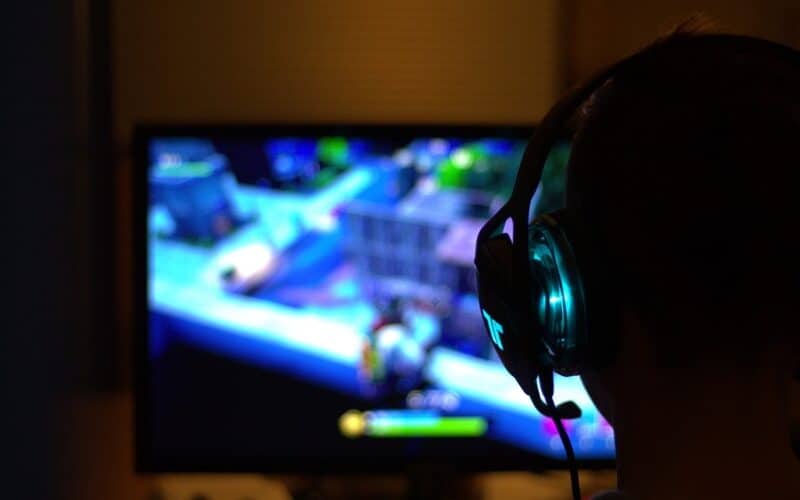 a smart tv with a game on its screen and a man with a headset seen from behind