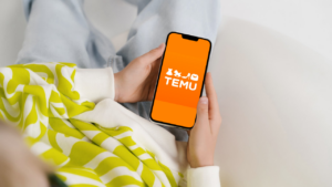 A person holding a smartphone displaying the Temu app logo, representing the top global mobile app market trends for May 2026.